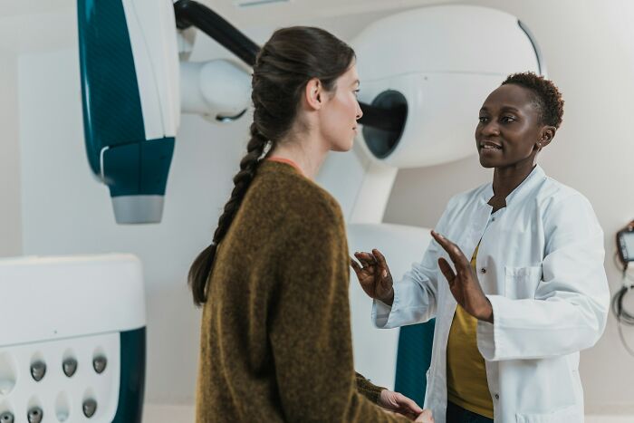 Doctor in white coat explaining medical procedure to female patient in hospital with advanced diagnostic equipment nearby