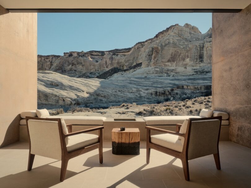 Two modern armchairs and a small table on a patio overlook a rocky desert landscape with large beige cliffs under a clear blue sky.