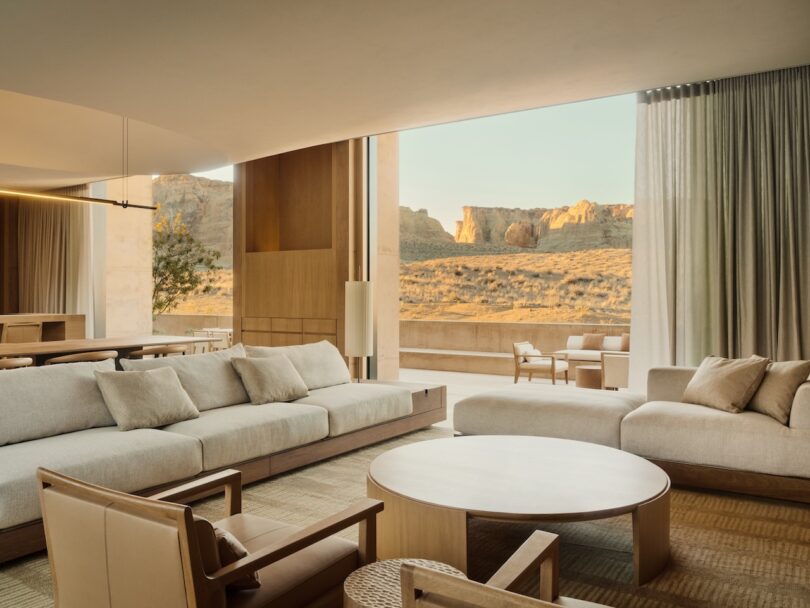 Modern living room with neutral-toned furniture, large windows, and a view of a desert landscape with rock formations outside.