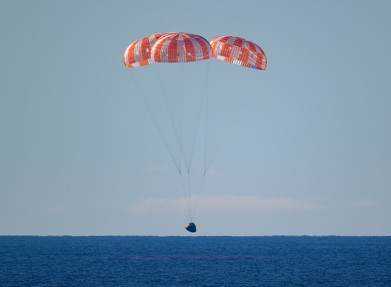 Integrity, dangling from three red and white parachutes, about to splash down in the Pacific Ocean.