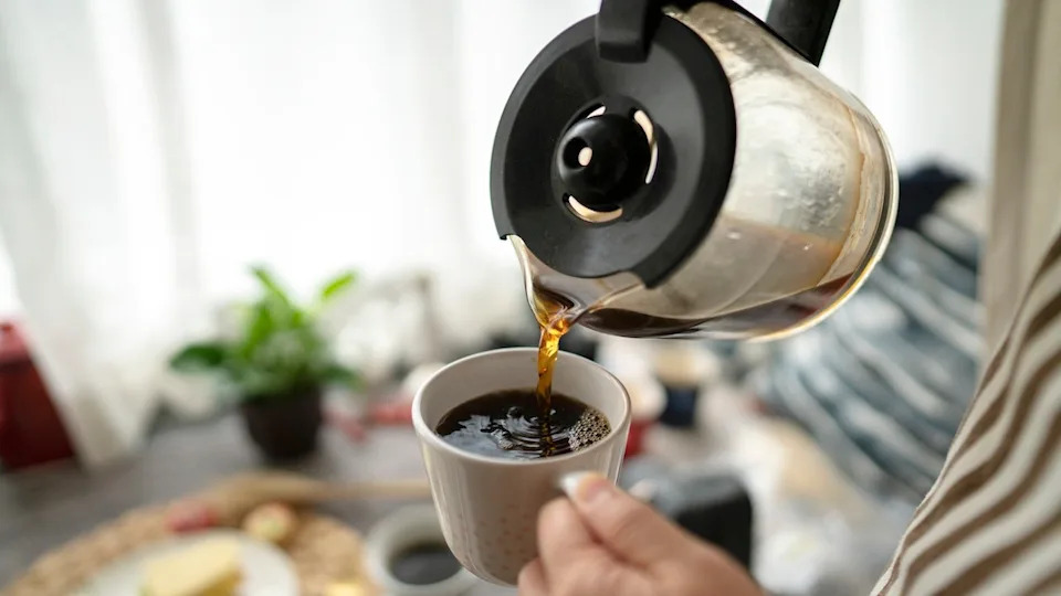 Young woman pouring coffee into a mug in front of a window