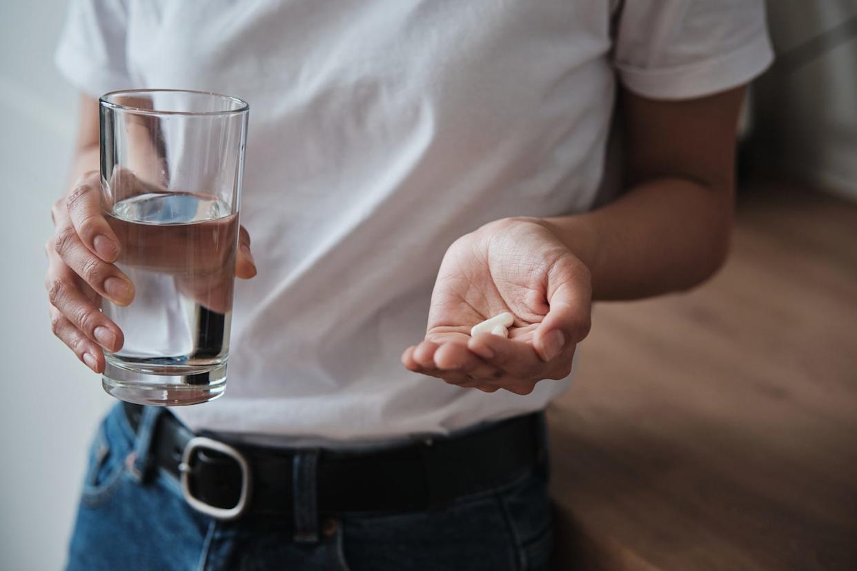 woman holding pills and glass of water while standing in kitchen at home, cropped photo, people taking vitamins daily, treating disease mental health medications, multivitamins and food supplements