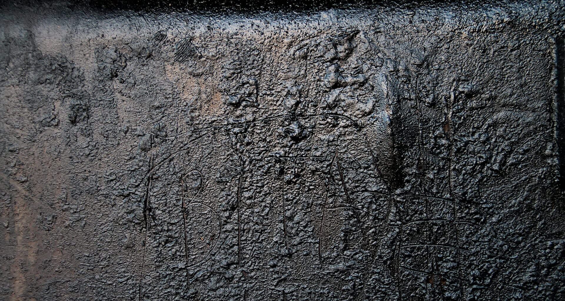 A textured black surface with a few faint scratches and markings.