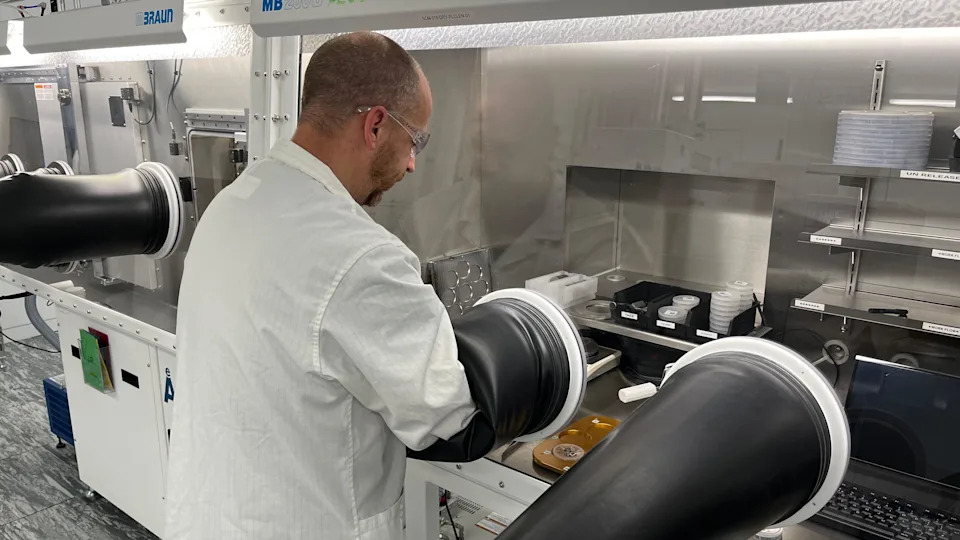 A man in a lab coat has his hands in an airtight container where he is processing products.