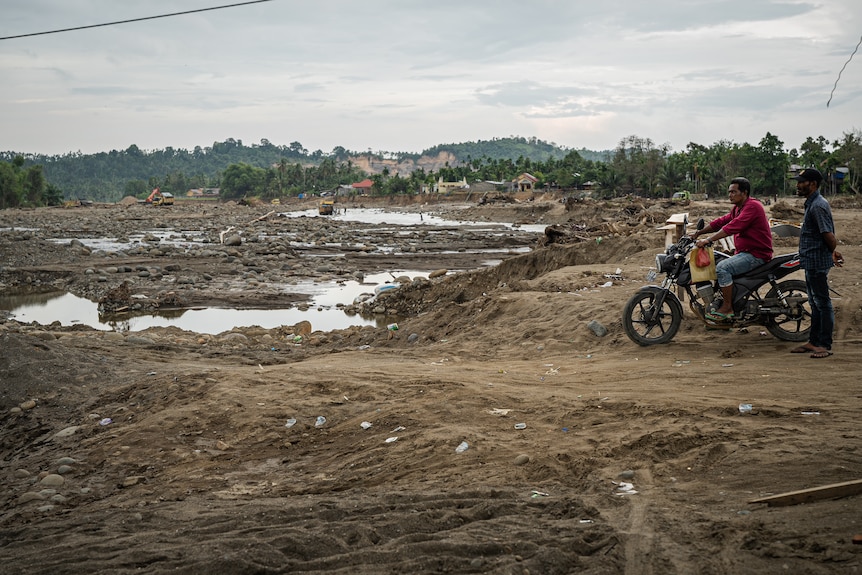 A family sitting on a motorcycle observing the destruction and damage.