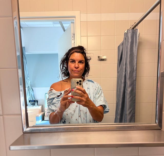A person in a medical setting taking a selfie in a mirror.