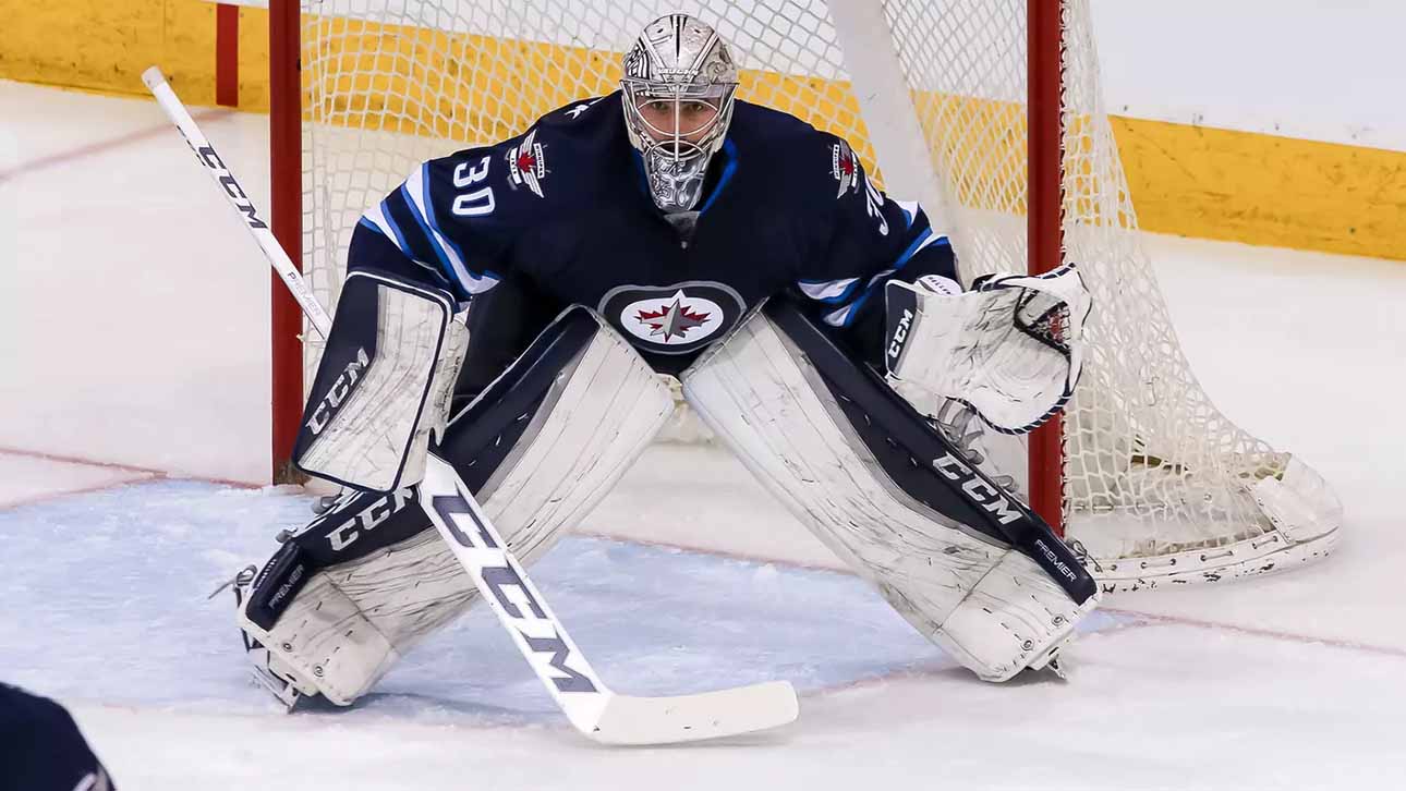Connor Hellebuyck, star goaltender for the Winnipeg Jets, in focused butterfly stance in full navy blue and white gear in front of the net during an NHL game, amidst recent trade rumors.