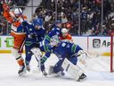 Anaheim Ducks' Alex Killorn (17) is struck by the puck while being checked by Vancouver Canucks' Tom Willander (5) in front of goalie Kevin Lankinen (32) as Linus Karlsson (94) checks Anaheim's Mikael Granlund (64) during the first period 