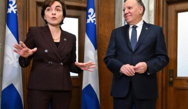 Christine Fréchette and François Legault stand and speak in front of doors and Quebec flags.