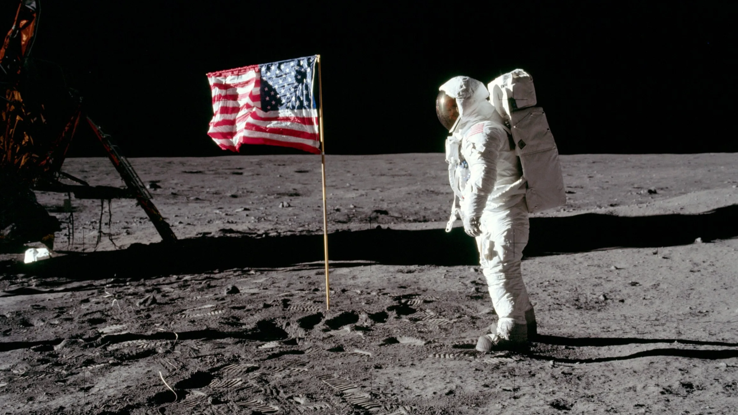 An astronaut is pictured on the moon's surface facing an American flag.