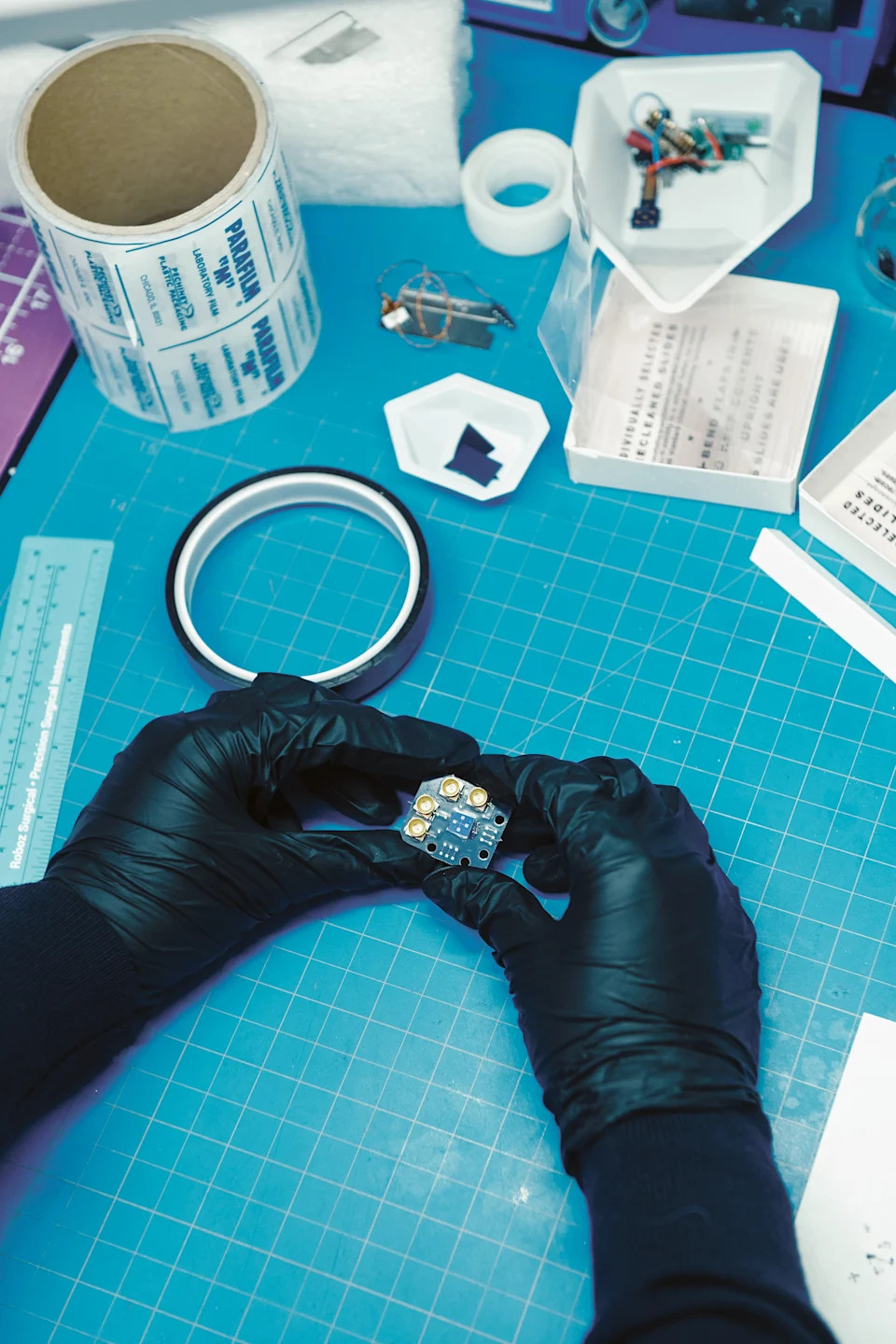 A person wearing black gloves holds a sample of the silicon chip over a blue table.