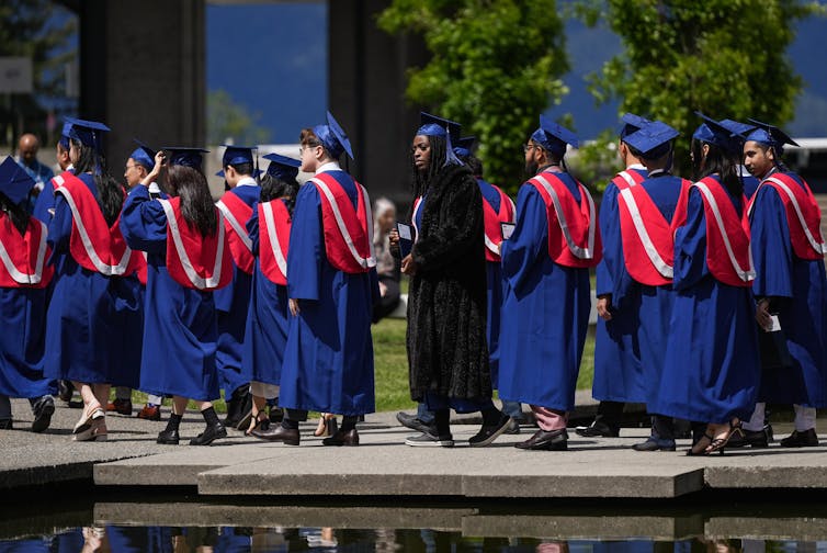 A line of young adults wearing graduuation robes walk along