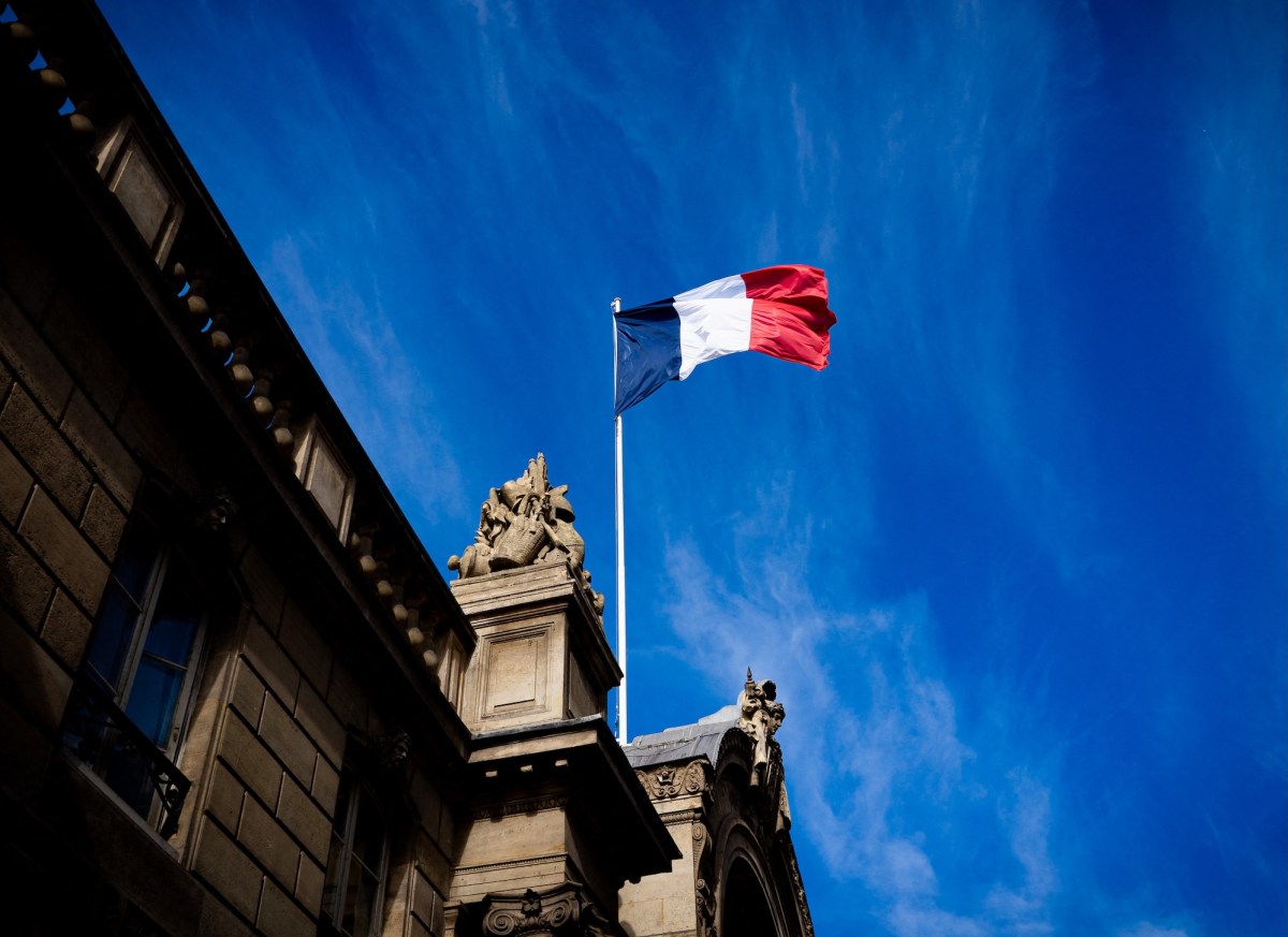French tricolour flag (blue, white and red, symbol of the Republic of France) hanging from a flagpole above the entrance gate to the courtyard of the Elysee Palace, Exit from the Cabinet meeting at the Presidential Palace of the Elysee in Paris, France on August 27, 2025. The ministers get into their cars and leave the Elysee Palace. (Photo by Amaury Cornu / Hans Lucas via AFP)