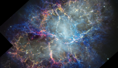 Colorful nebula in space with a white haze throughout that is more concentrated in the center with a rippling effect. Colorful gas filaments appear to splash outward from the nebula center, colored yellow, magenta, and blue. A faint black border with right angles at the corners of the images show where the telescope’s field of view stops. Small white stars dot the background.