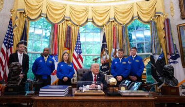 four people in blue flight jackets stand behind an old man at a desk in a grotesquely decorated office