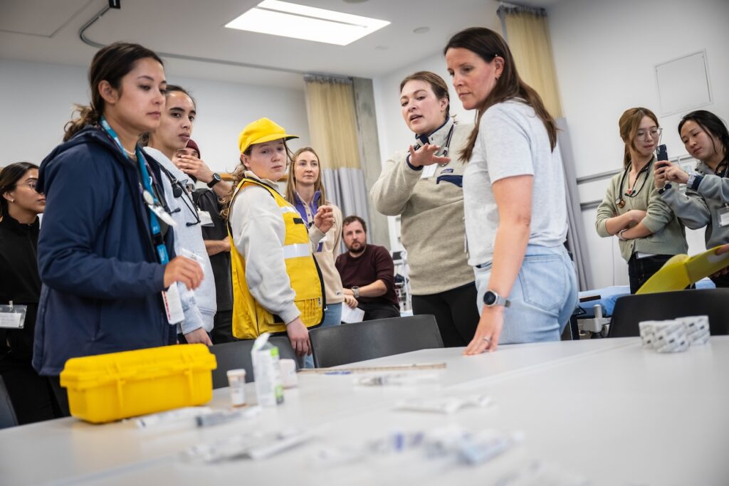 Emergency medicine resident doctors discuss inventory of supplies on a table in a medical room.