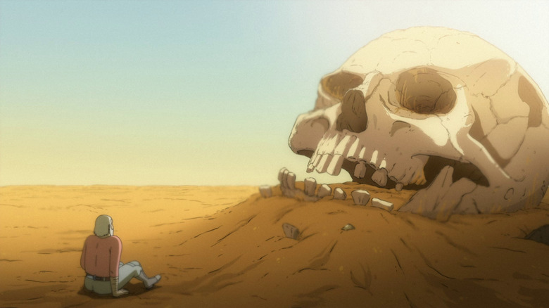 Sam sitting in front of a giant human skull in the sand