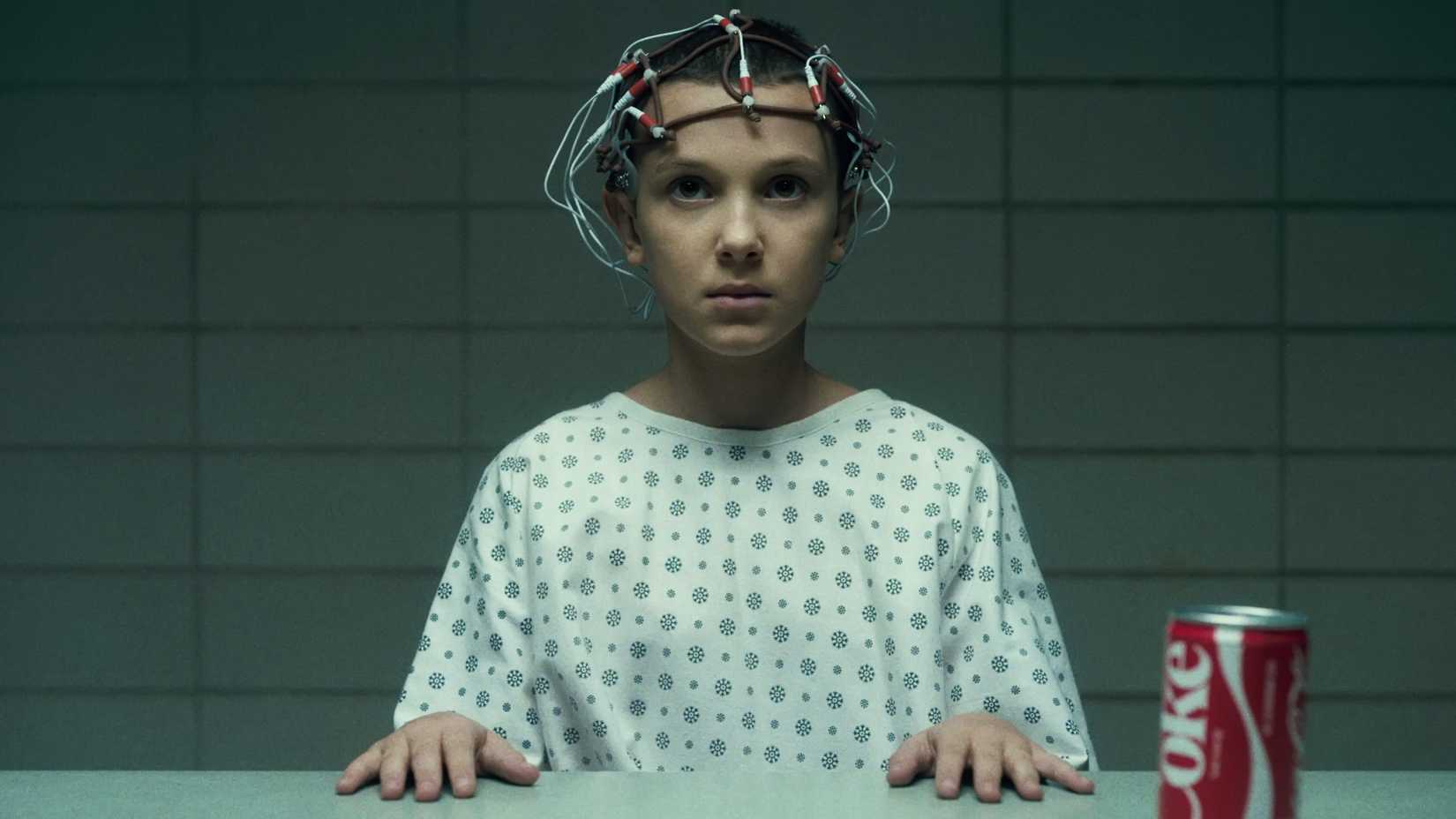 Eleven (Millie Bobby Brown) with scientific equipment attached to her head as she's observed at Hawkins Lab in Stranger Things season 1