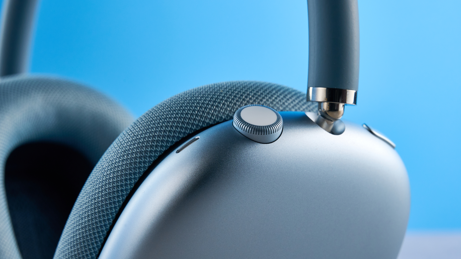 the apple airpods max 2 in blue photographed against a blue tom's guide background, showing the mesh headband, anodized aluminum ear cups, carry case, and controls