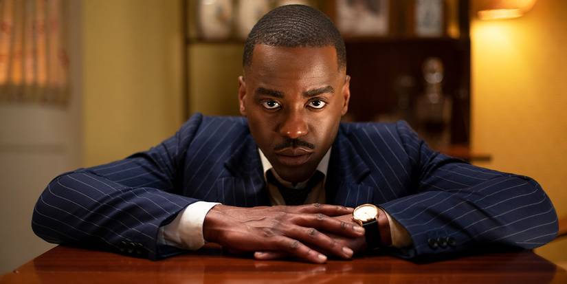 Ncuti Gatwa in a pinstriped suit leaning on a table and staring down the lens in Doctor Who.