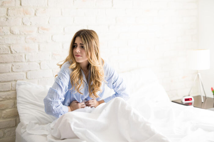 Young woman in pajamas sitting in bed holding her stomach, illustrating patients' confessions while under sedation.