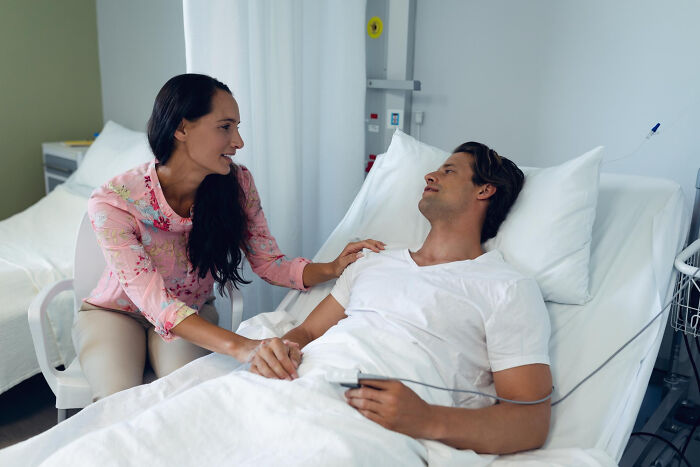Woman comforting a male patient in hospital bed, illustrating surgical staff and unhinged patient confessions under sedation.