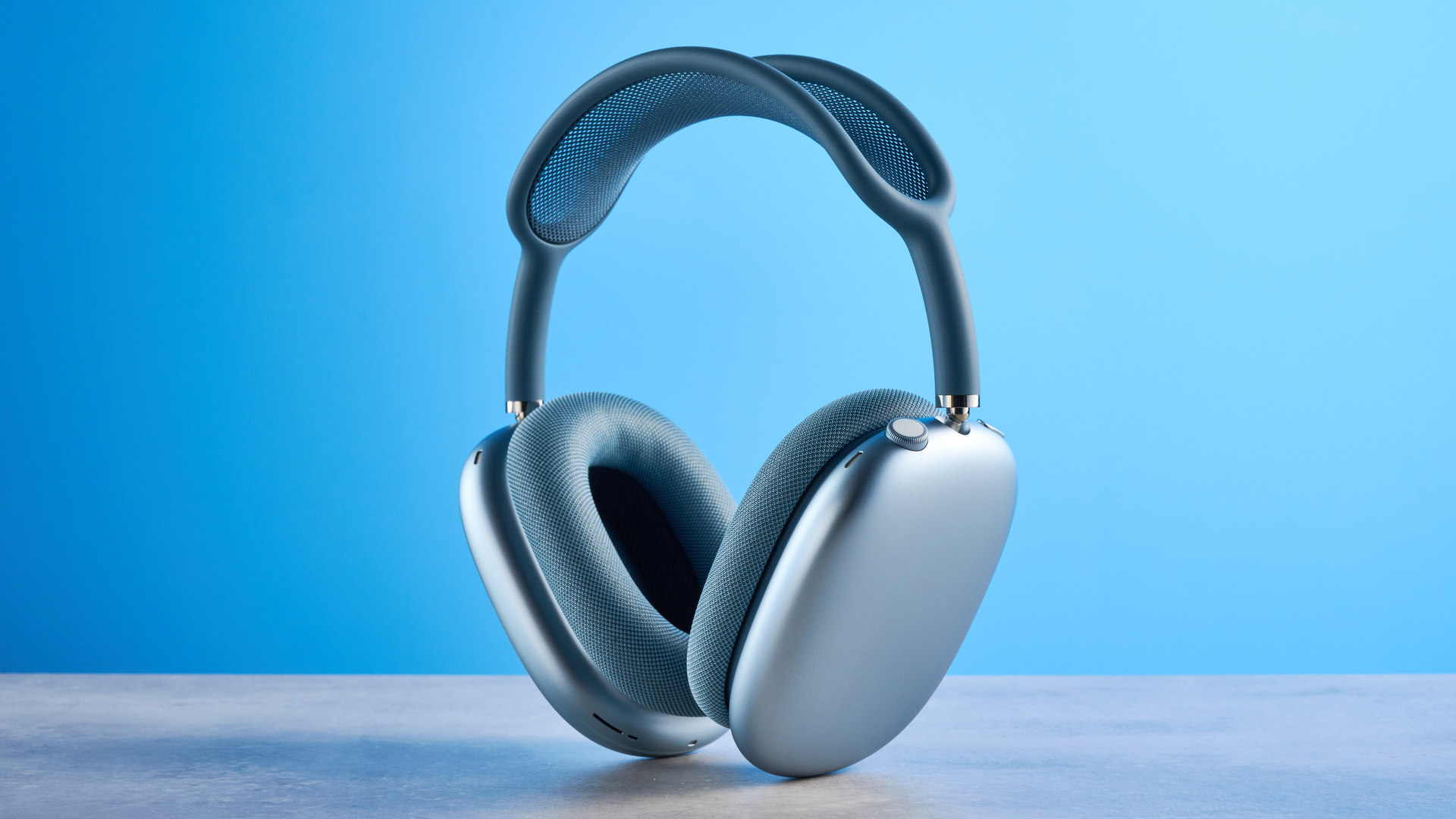 the apple airpods max 2 in blue photographed against a blue tom's guide background, showing the mesh headband, anodized aluminum ear cups, carry case, and controls