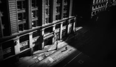 a black-and-white photograph by Daniel Sackheim in a noir style of an elevated city street view with a figure walking amid deep shadows