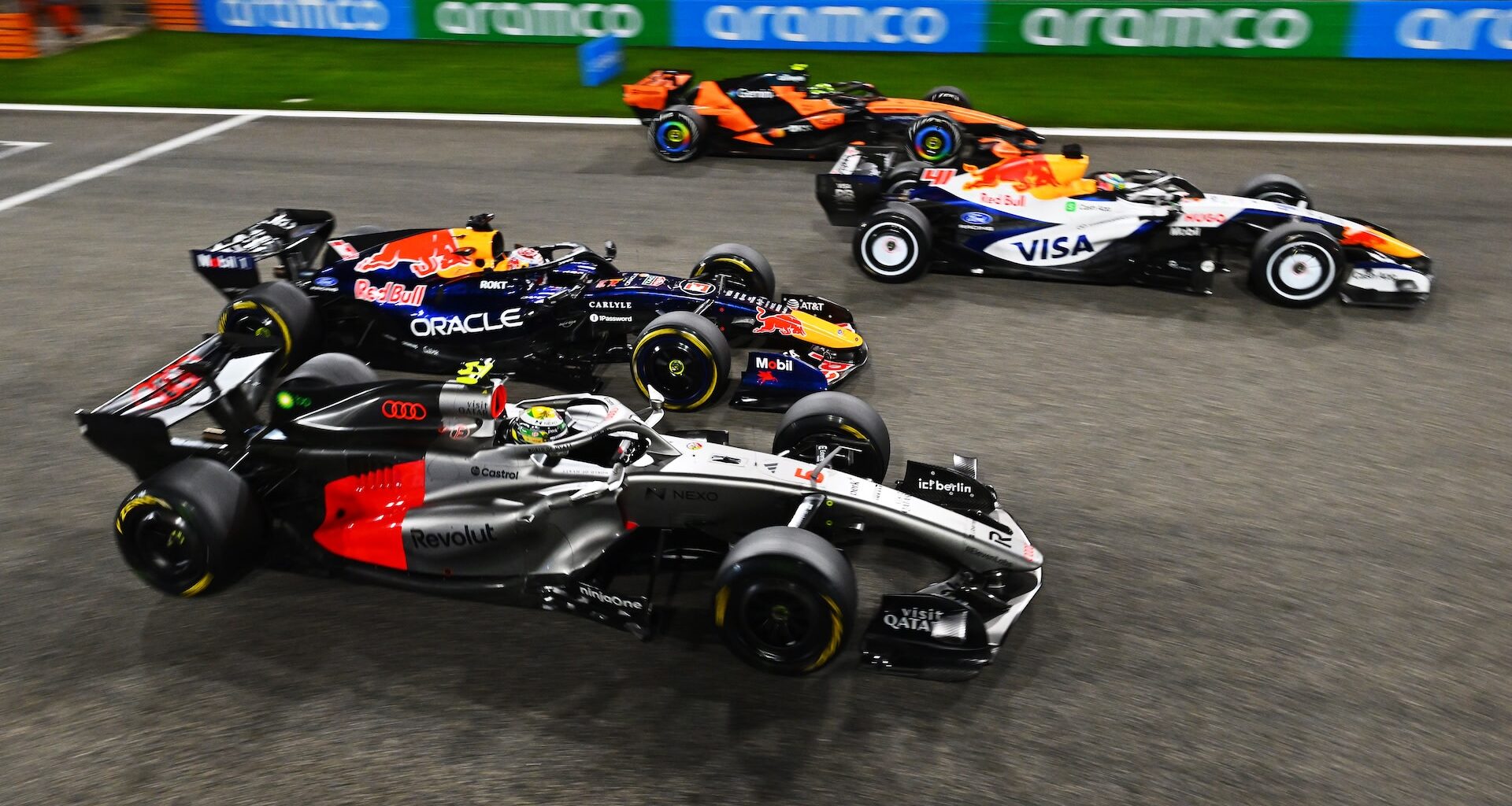 Four Formula 1 cars racing on a track, showcasing vibrant team liveries and sponsorship logos.