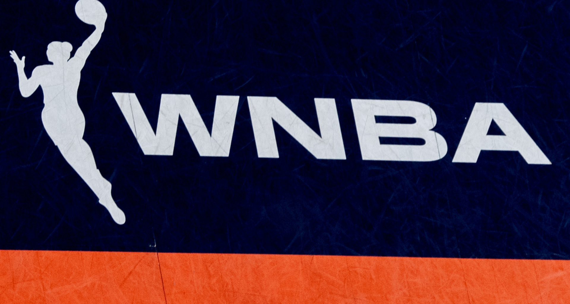 WNBA logo with a silhouette of a female basketball player in action, set against a dark blue and orange background.
