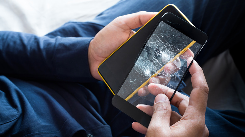 A man holding a smartphone and a damaged tempered glass