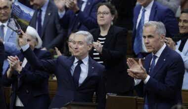 François-Philippe Champagne holds up a book while Mark Carney and other MPs applaud in the House of Commons.