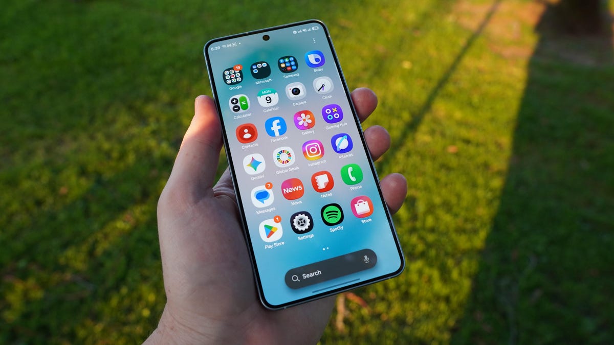 A phone held face up with apps on screen showing and park grass behind it.