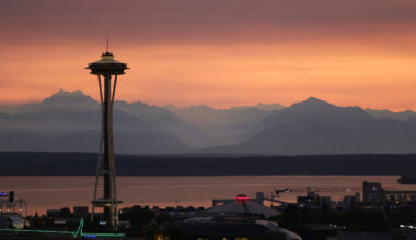Seattle’s Space Needle is seen at dusk, with mountains and an orange sky in the background.