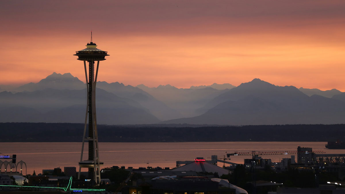 Seattle’s Space Needle is seen at dusk, with mountains and an orange sky in the background.