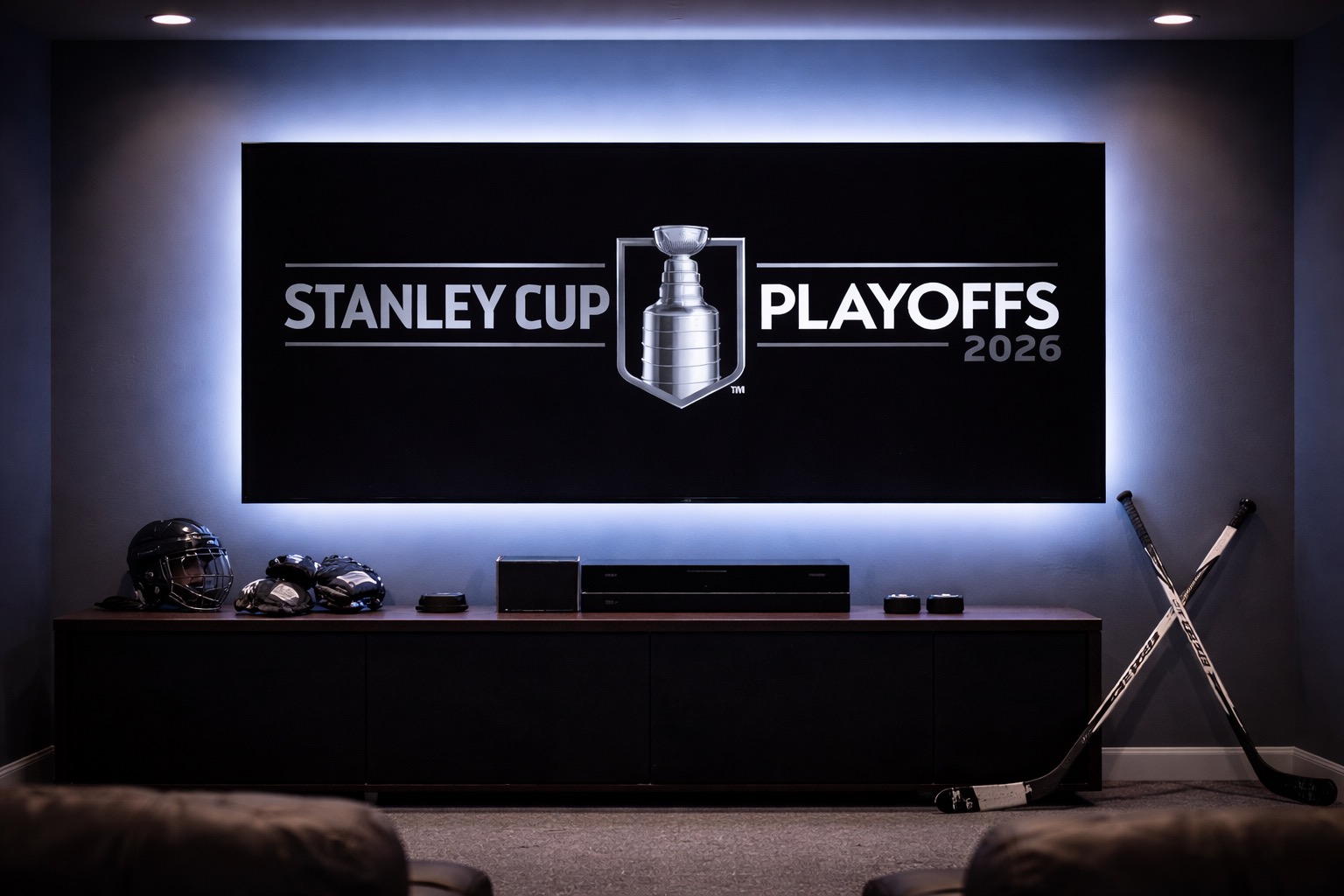 Home theater scene with a large TV displaying the Stanley Cup Playoffs 2026 logo, blue ambient light, and hockey gear on a cabinet beneath.