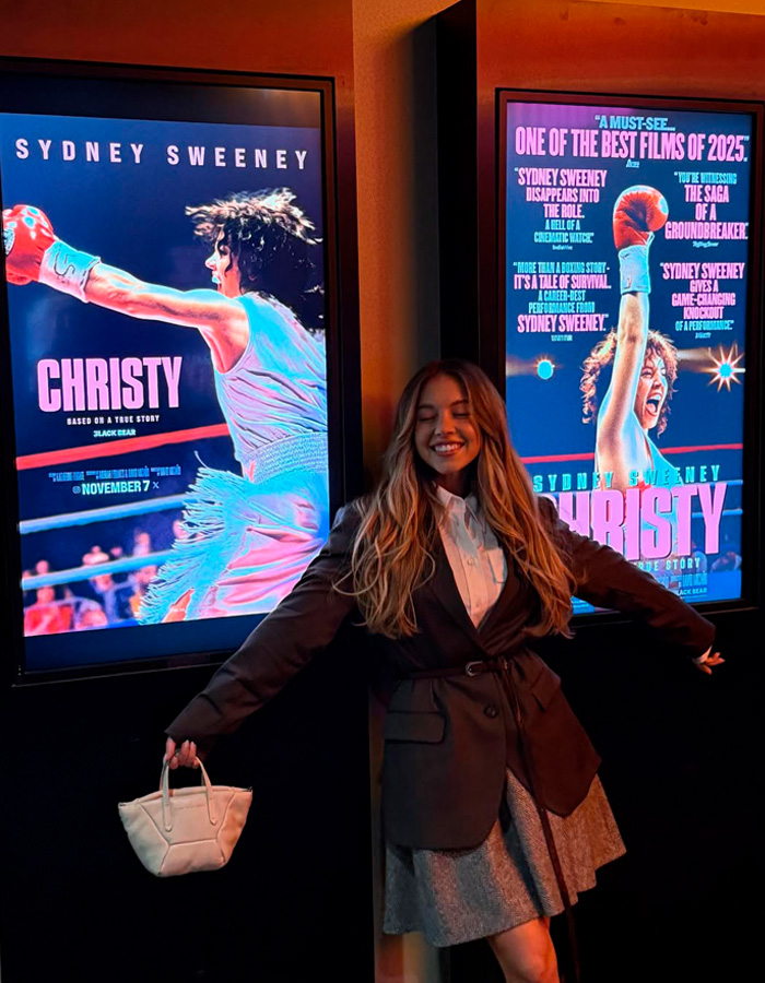 Young woman smiling and posing happily in front of movie posters featuring Sydney Sweeney in Christy.