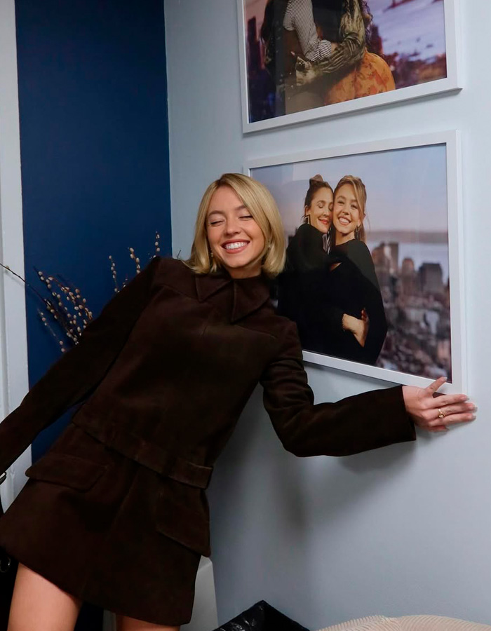 Sydney Sweeney smiling and posing beside framed photos, capturing a moment linked to exposing influencer’s lie.