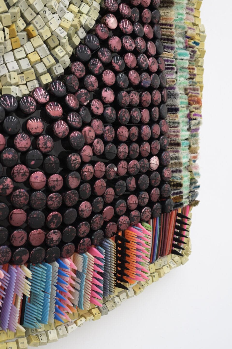 a detail of an abstract wall-installed artwork by Moffatt Takadiwa made from computer keyboard keys, combs, toothbrush heads, and pieces of nail polish applicators