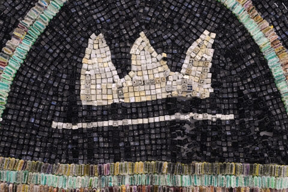 a detail of an abstract wall-installed artwork by Moffatt Takadiwa made from computer keyboard keys, combs, toothbrush heads, and pieces of nail polish applicators