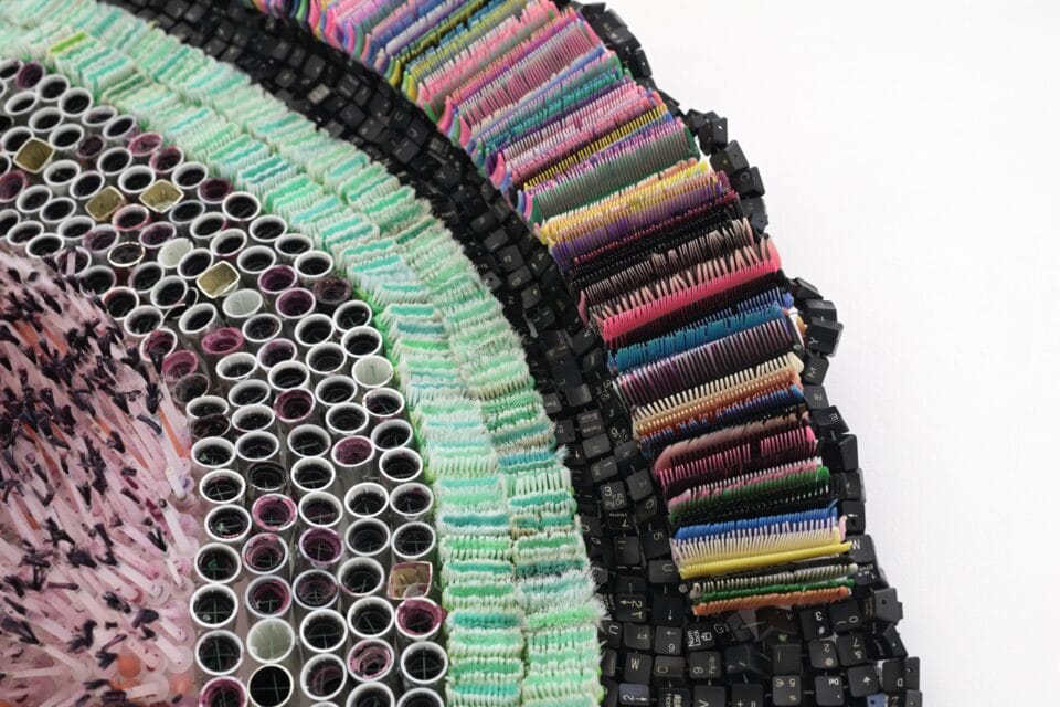 a detail of an abstract wall-installed artwork by Moffatt Takadiwa made from computer keyboard keys, combs, toothbrush heads, and pieces of nail polish applicators