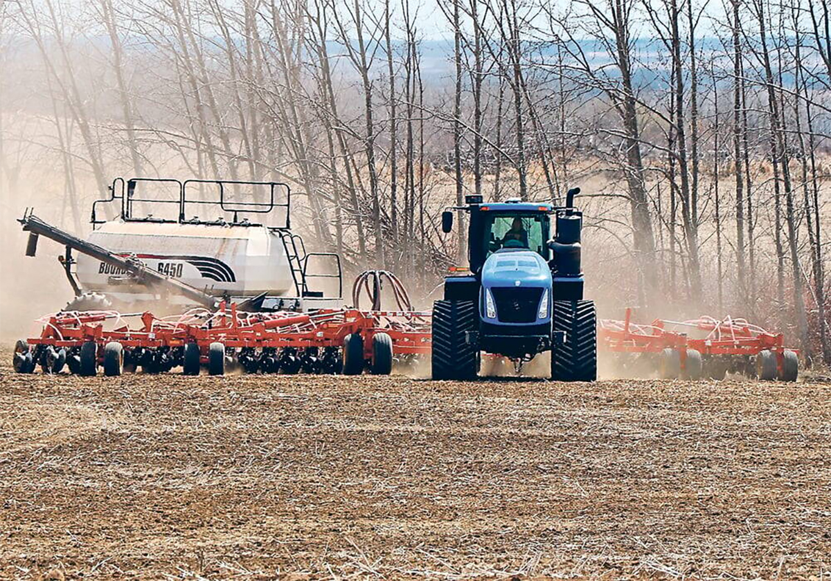 A large, blue, tracked tractor is pulling an air seeding rig toward the camera.