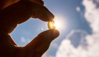 Yellow soft shell D-vitamin capsule against sun and blue sky on sunny day.