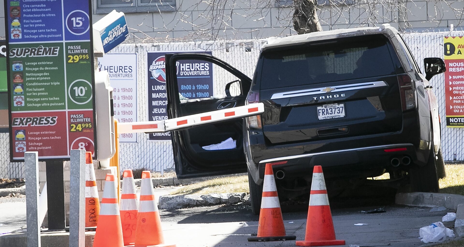 An SUV is behind orange safety cones at a car wash. The door is open and the SUV is partially over a curb.