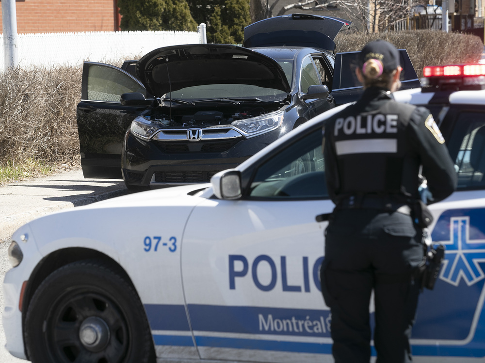 A police officer stands next to a police vehicle, looking toward a black SUV that has its doors, trunk and hood open.