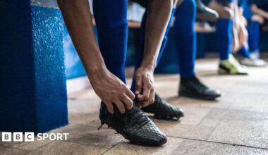 Soccer player tying shoelaces while preparing for match in the locker room