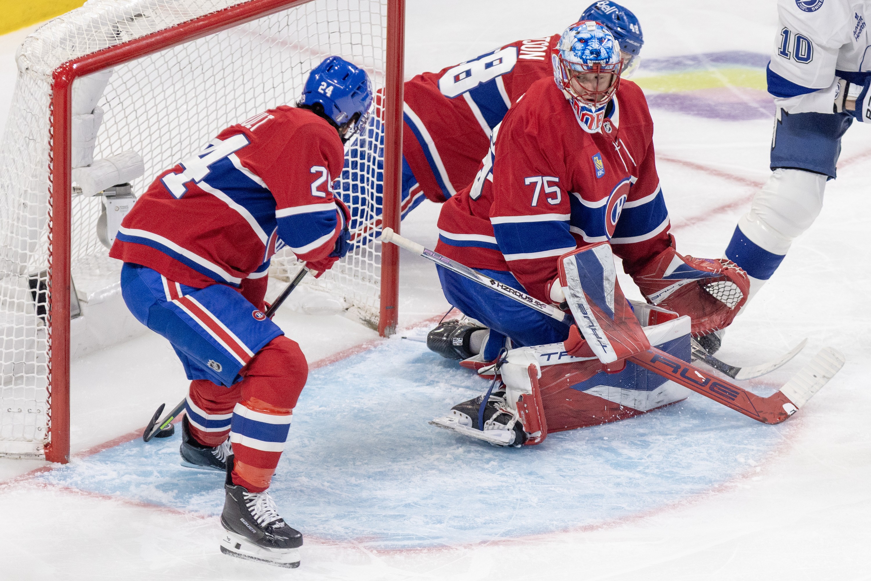 Hockey player reaches back to keep the puck from crossing the goal line.