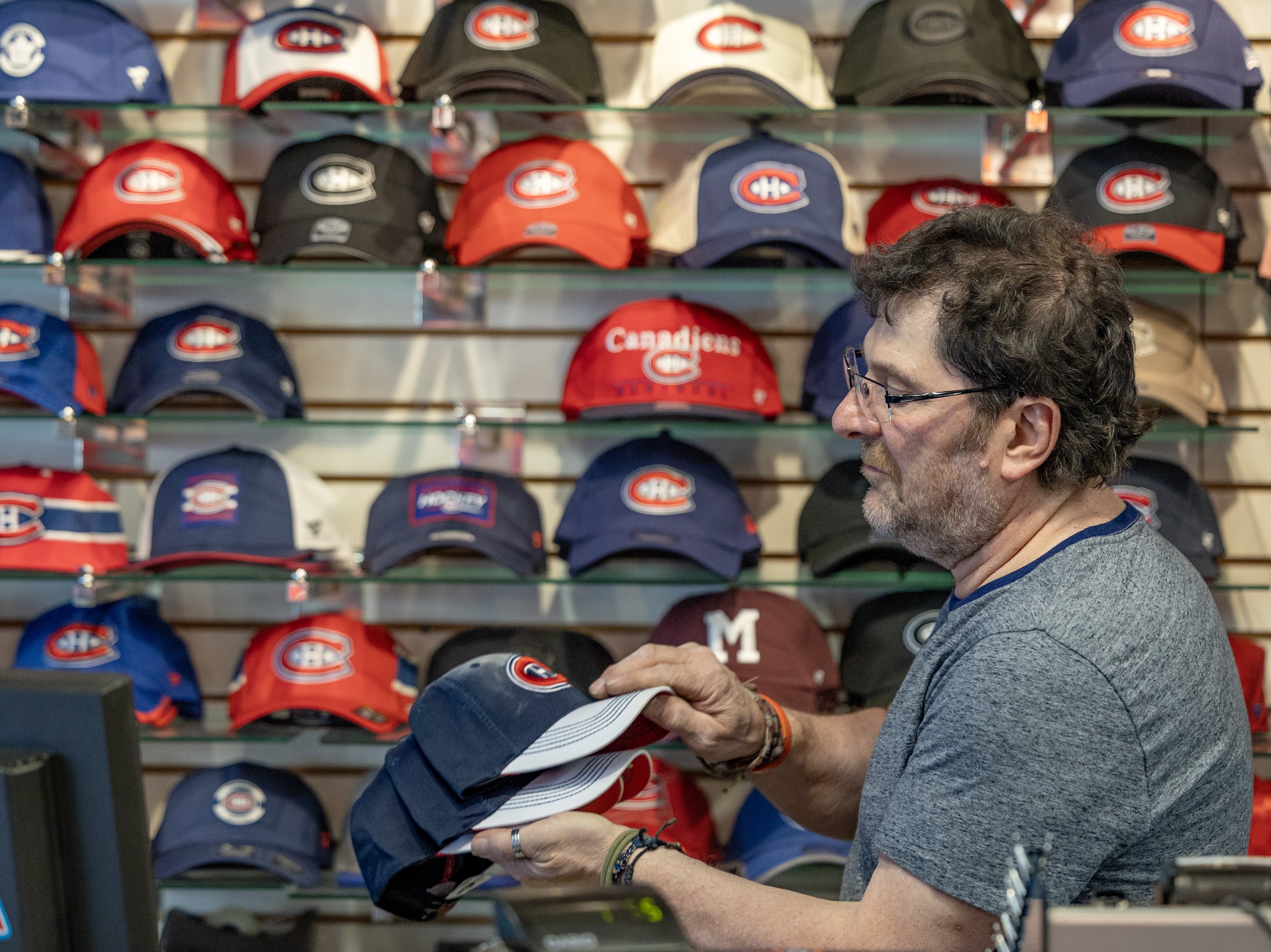 A man places baseball-style hats on a wall display inside a store.