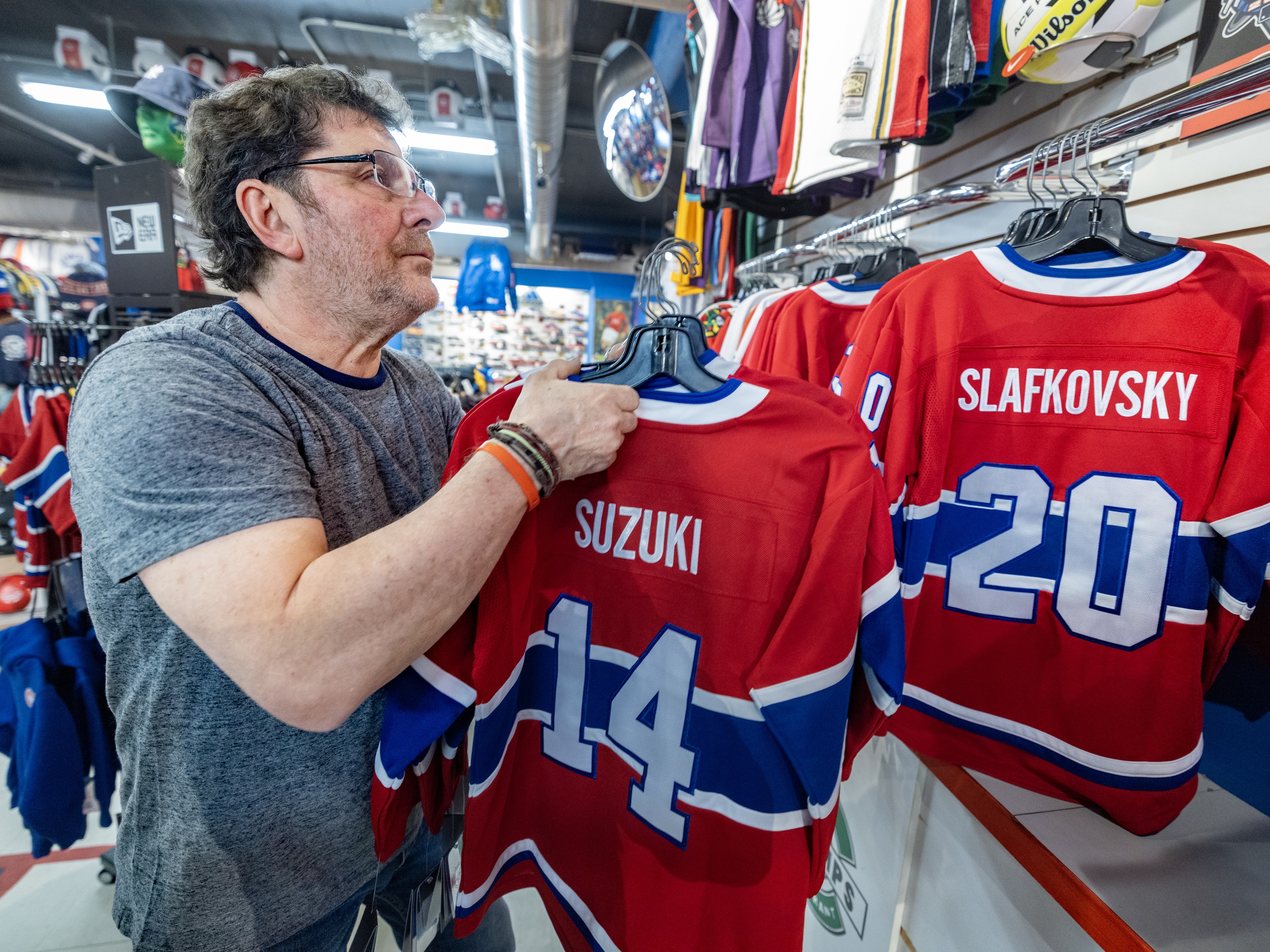 A man hangs Canadiens jerseys on a rack inside a store.