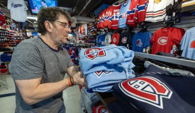 Tony Araujo holds a pile of light blue Canadiens hoodies above a shelf in a sports apparel store.